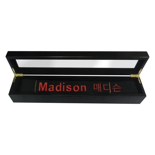 Black rectangular belt display case with gold hinges containing black scroll embroidered madison in red and korean script